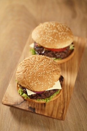 two homemade burgers on olive board on oak table, shallow focusの写真素材