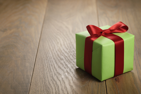 simple green paper gift box with red ribbon bow on oak table with copy space, shallow focusの写真素材
