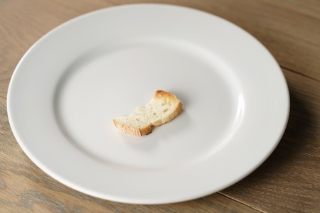 white plate with single dry slice of baguette bread, focus on breadの写真素材