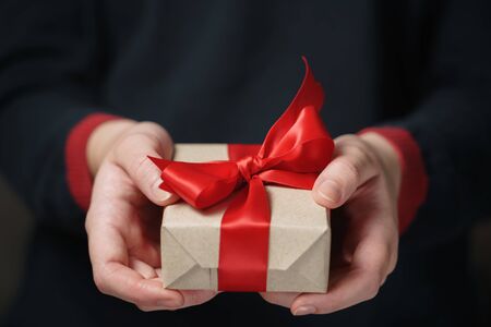 female teen hands show craft paper gift box with red bow, shallow focus
