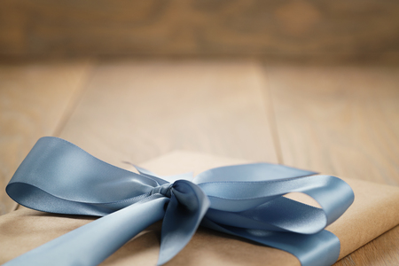 handmade gift brown paper box with blue ribbon bow on wood table, closeup photoの写真素材