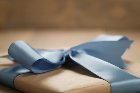 handmade gift brown paper box with blue ribbon bow on wood table, closeup photoの写真素材
