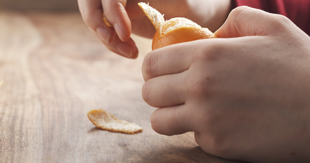 young female hand peels clementine tangerine on wooden table, 4k photoの写真素材