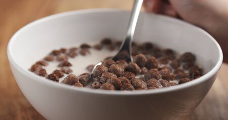 closeup of cereal chocolate balls with milk in white bowl on wood table
