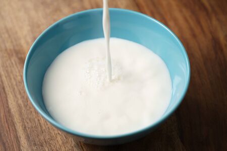 fresh milk poured into blue bowl on wood table, organic foodの写真素材
