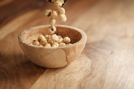 roasted hazelnuts falling in wood bowl on wooden table, copy space on the right sideの写真素材