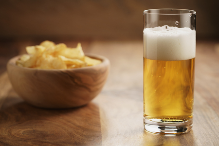 glass of lager beer with potato chips on wooden table, focus on beerの写真素材