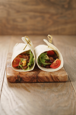 homemade tortilla wrap sandwiches with beef and vegetables on olive board, closeup photo with shallow focusの写真素材