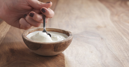 eating organic yogurt with spoon from wood bowl, 4k photo