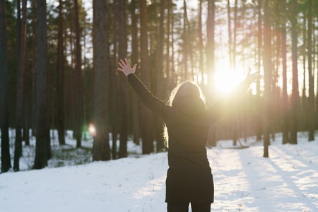 teen girl raised hands from behind in winter pine forest in sunset, freedom or victory conceptの写真素材