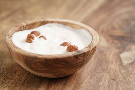 homemade yogurt with hazelnuts in wood bowl on wooden table, shallow focusの写真素材