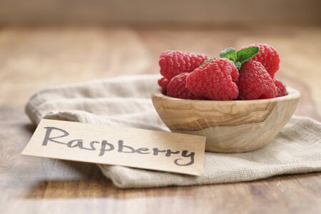 bowl with raspberries with paper card on wood table, simple photo