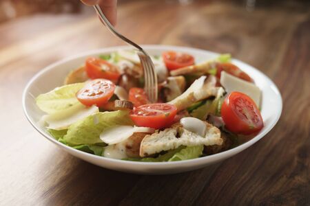 eating caesar salad with chicken and cherry tomatoes on wood table, shallow depth of fieldの写真素材