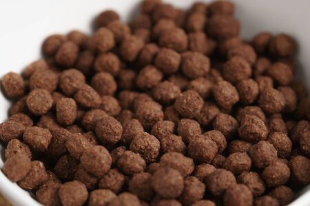 closeup of chocolate cereal balls in white bowl for breakfast on wooden table, shallow focus