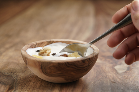 eating with spoon homemade yogurt with muesli in wood bowl on wooden table, shallow focusの写真素材