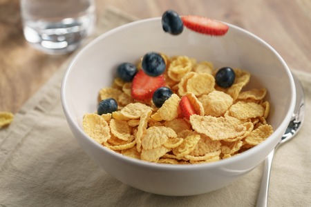 berries falling into corn flakes for breakfast in bowl on table