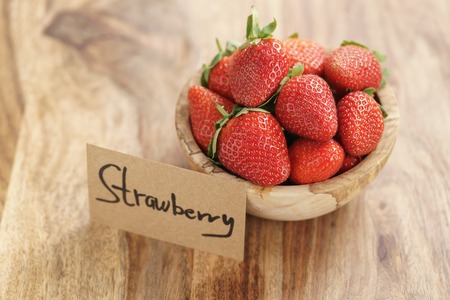 bowl with strawberries with paper card on wood table, organic garden berriesの写真素材