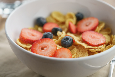 closeup of dry corn flakes with berries in bowl, breakfast preparation
