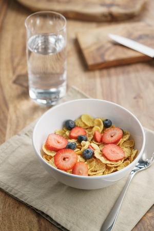 dry corn flakes with berries in bowl on table, breakfast preparation