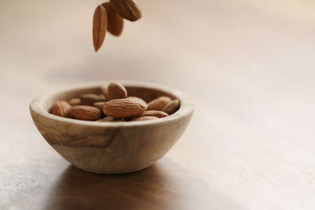 roasted almonds falling in wood bowl on wooden table, closeup photoの写真素材
