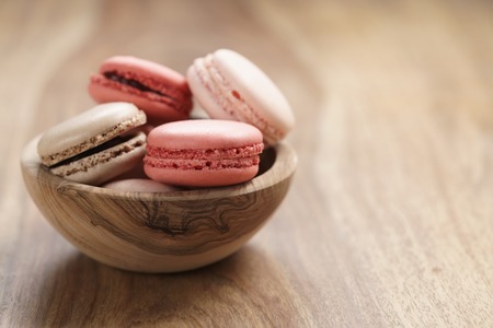 pastel colored macarons with strawberry, rose and caramel flavour in wood bowl with copy spaceの写真素材