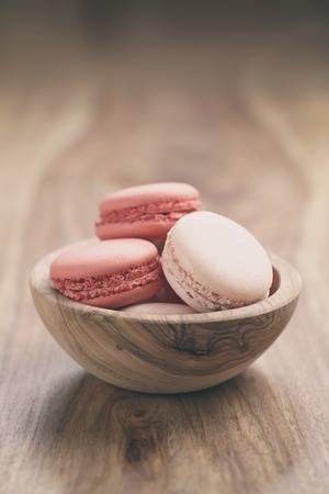 pastel colored macarons with strawberry and rose flavour in wood bowl on table vintage tonedの写真素材