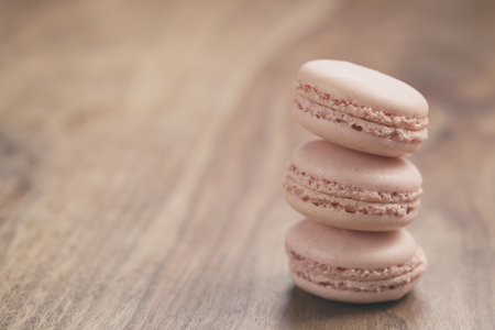 closeup shot stack of pastel colored macarons with rose flavour on wood table, vintage toned photoの写真素材