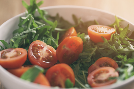 cherry tomatoes with arugula salad in white bowl on wooden table, vintage toned photoの写真素材