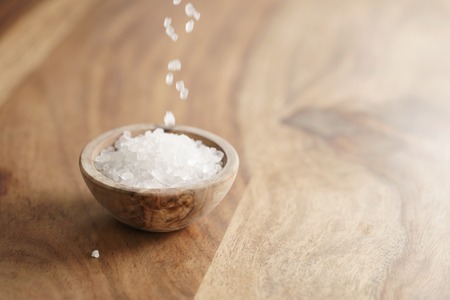 coarse sea salt falling into wooden bowl on table, with copy spaceの写真素材
