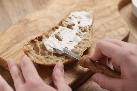 spreading ricotta cheese on fresh rustic bread, shallow focus
