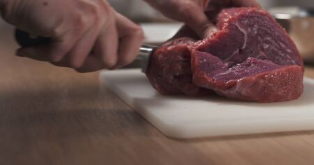young female hand cutting raw beef with a knife on plastic board, 4k photo