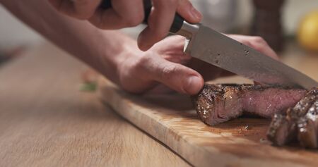 man slicing cooked medium rib eye steak on board, wide photo
