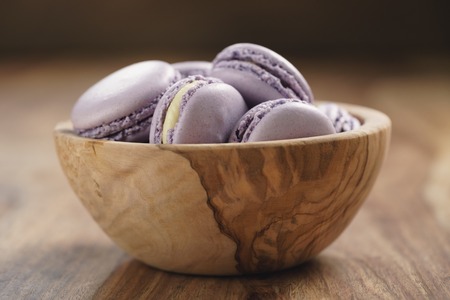 violet macarons in wood bowl on wooden table, closeupの写真素材