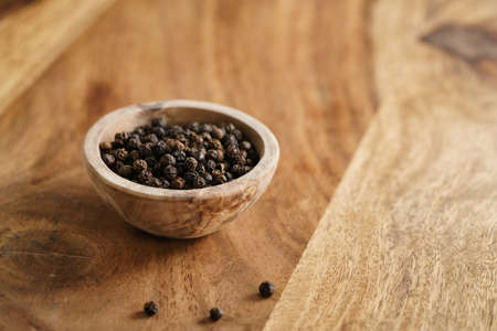 black dry pepper in wooden bowl on tableの写真素材