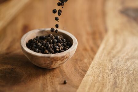 black dry pepper fall into wooden bowl on tableの写真素材