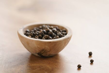 black dry pepper in wooden bowl on table, with copy spaceの写真素材