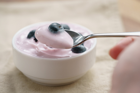 pov teen girl hand eating organic blueberry yogurt, shallow focusの写真素材