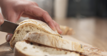 young female hands slicing ciabatta with olives on cutting board