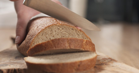 young female hands slicing rye wheat rustic bread on cutting board