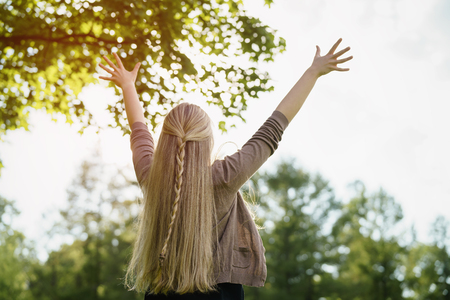 female teen girl stand in park feel freedom with arms stretched to the skyの写真素材