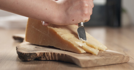 female hand cutting hard parmesan cheese, wide photoの写真素材