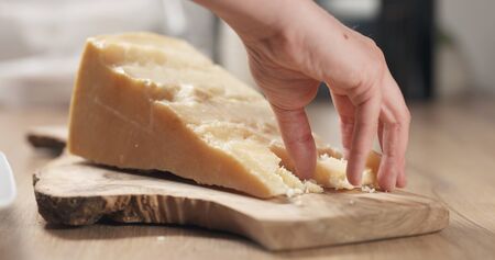 female hand taking pieces of hard parmesan cheese from olive board, wide photoの写真素材