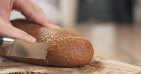 young female hands slicing rye wheat rustic bread on cutting board, wide photoの写真素材