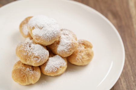 Closeup shot of profiteroles covered with sugar powder on white plate on wooden table, shallow focusの写真素材