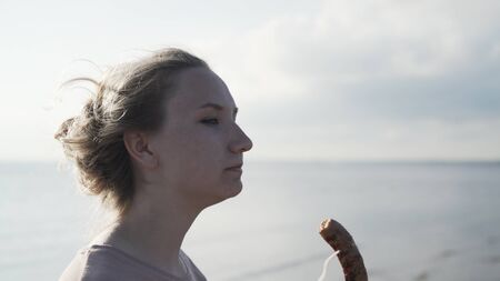 handheld shot of teen girl eating grill sausage on a beachの写真素材