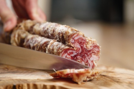 closeup shot of slicing salami with knife, shallow focus
