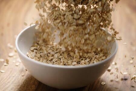 oat flakes fall in white bowl on wood tableの写真素材