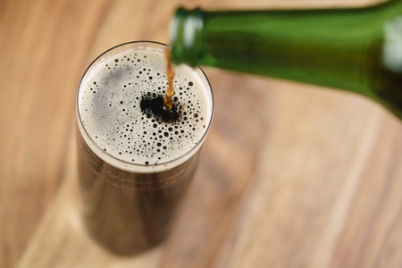 dark beer pouring in glass on wood table from aboveの写真素材