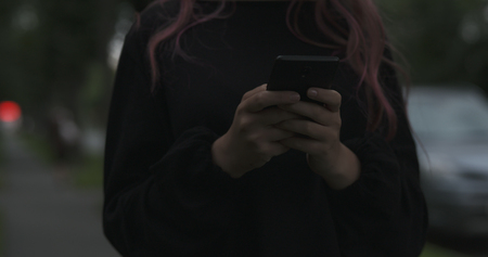 female teen using smartphone on the street at night, wide photoの写真素材
