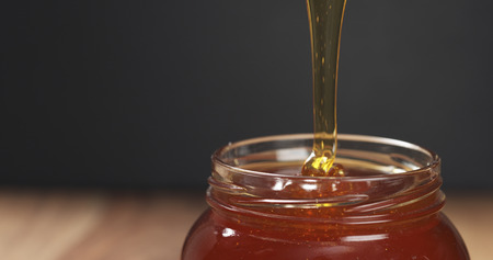 honey pour with spoon in glass jar, wide photoの写真素材